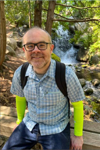 Picture of Loft staff member Chris Jones smiling in front of a waterfall