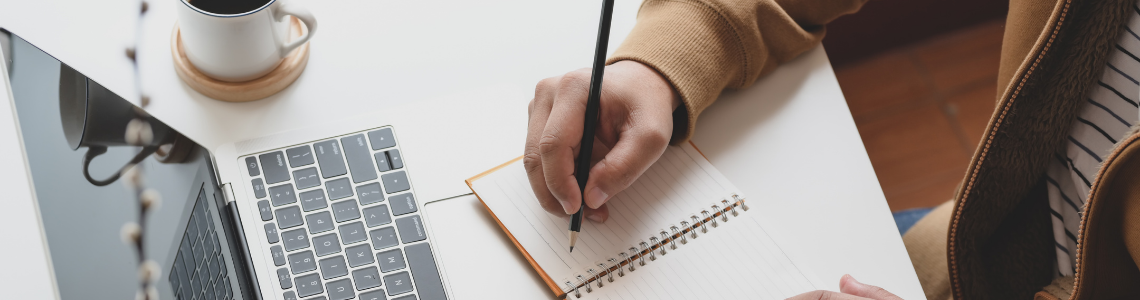 Banner image of a person writing in a notebook in front of a laptop