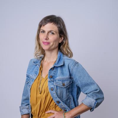 Person in yellow overalls and blue denim jacket against gray background
