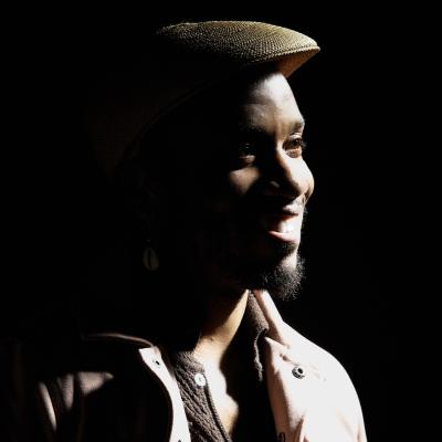 Portrait of Donte Collins in dramatic side light, wearing a hat and looking to the side.