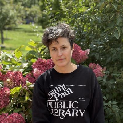 Portrait of Kara Olson standing outdoors in front of pink flowers and greenery.