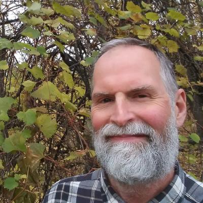 Portrait of Yahya Frederickson outdoors in front of leafy branches.