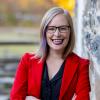 Woman in red jacket smiling against yellow backdrop outdoors.