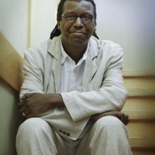 Portrait of Cornelius Eady seated on a staircase, wearing a light suit.