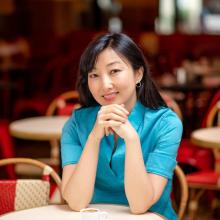 Portrait of Helena Ku Rhee seated at a café table, hands clasped, with a small cup in front of her.