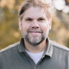 Man in green flannel against woodsy background