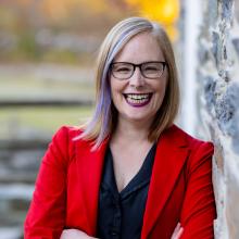 Woman in red jacket smiling against yellow backdrop outdoors.